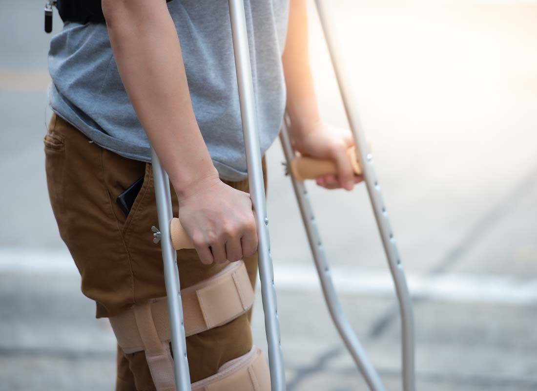 Disability Insurance - Close-up of Woman’s Lower Body and Knee Support Using Crutches Standing and Trying to Walk after Suffering a Work Related Injury