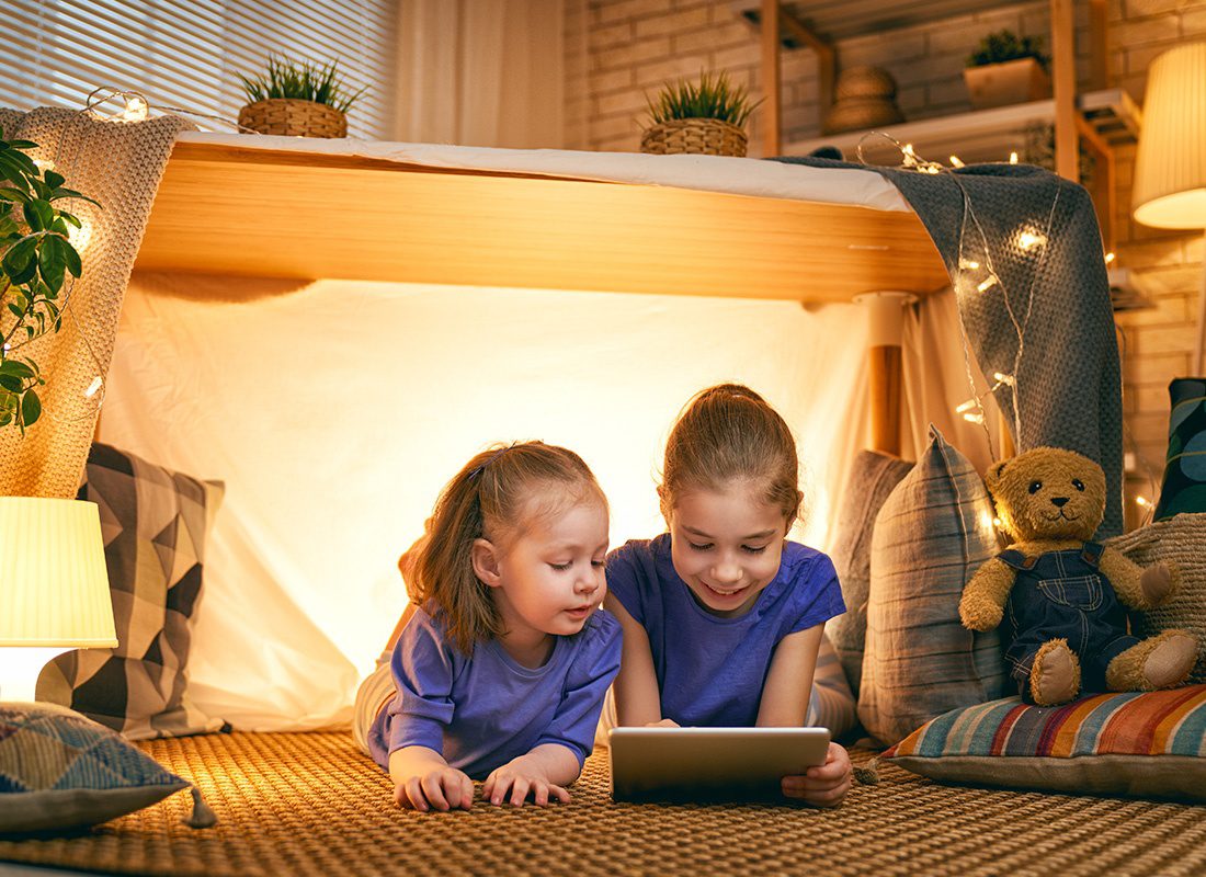 Blog - Two Little Girls Lay Inside a Tent With Lights While Looking at a Tablet at Home